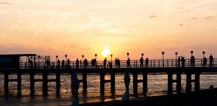 LAZAREVSKOE, SOCHI, RUSSIA - MAY, 26, 2021: Orange saturated sunset with silhouettes of people on the background of the sun.