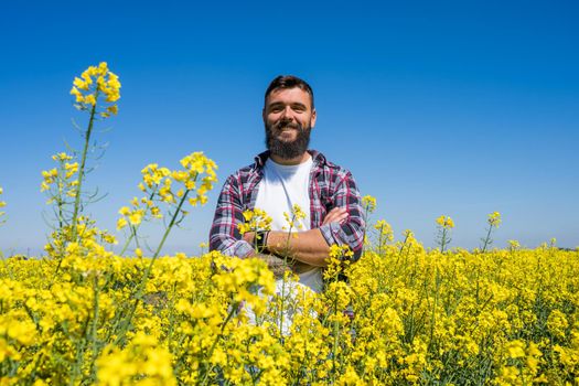 Portrait of happy and successful farmer who is standing by his rapeseed field. Rapeseed plantation in bloom.