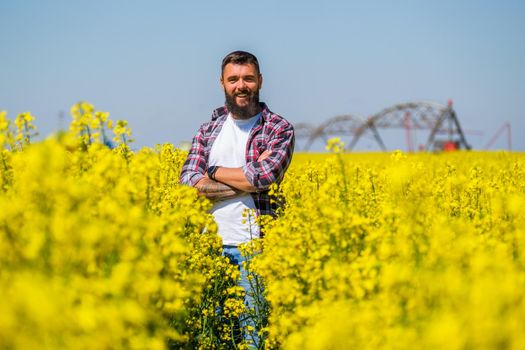 Portrait of happy and successful farmer who is standing in his rapeseed field. Rapeseed plantation in bloom.