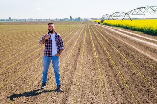 Happy farmer is standing in his sown corn field. He is satisfied with quality of his land.