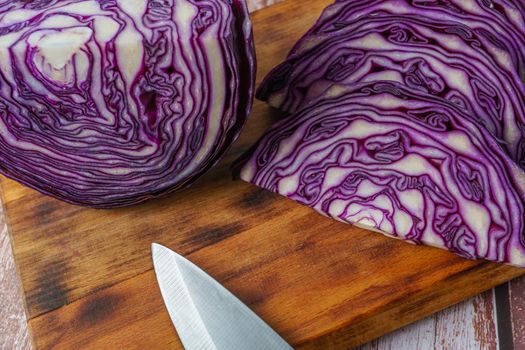 close-up of a red cabbage or purple cabbage cut with a knife on a wooden board