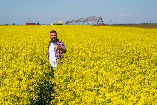 Portrait of happy and successful farmer who is standing in his rapeseed field. Rapeseed plantation in bloom.