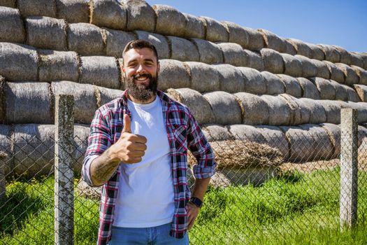 Happy farmer is standing beside bales of hay.