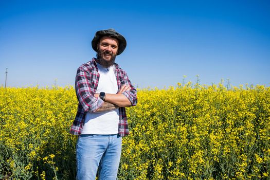 Portrait of happy and successful farmer who is standing by his rapeseed field. Rapeseed plantation in bloom.