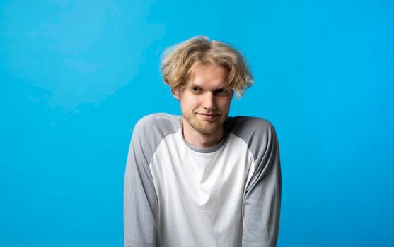 Portrait of young man in long sleeve t-shirt smiling looking at camera over blue background studio. Emotions