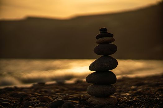 Pebble pyramid silhouette on the beach. Sunset with sea in the background. Zen stones on the sea beach concept, tranquility, balance. Selective focus.