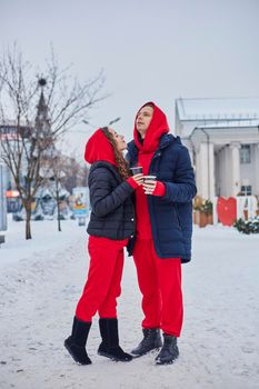 young family guy and girl spend the day in the park on a snowy day. the guy hugs the girl while standing on the street, they drink coffee together