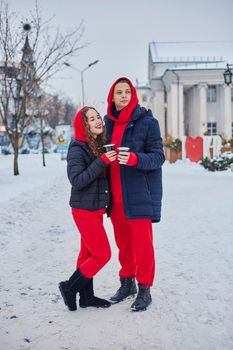 young family guy and girl spend the day in the park on a snowy day. the guy hugs the girl while standing on the street, they drink coffee together