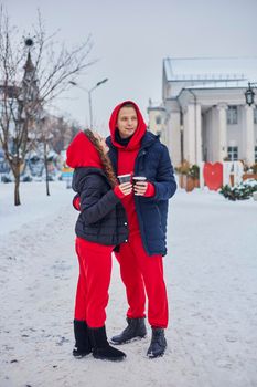 young family guy and girl spend the day in the park on a snowy day. the guy hugs the girl while standing on the street, they drink coffee together