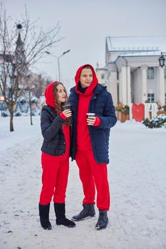 young family guy and girl spend the day in the park on a snowy day. the guy hugs the girl while standing on the street, they drink coffee together