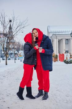 young family guy and girl spend the day in the park on a snowy day. the guy hugs the girl while standing on the street, they drink coffee together