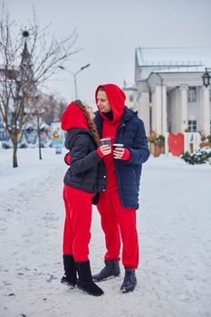 young family guy and girl spend the day in the park on a snowy day. the guy hugs the girl while standing on the street, they drink coffee together