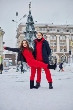 young family guy and girl spend the day in the park on a snowy day. Emotional young couple having fun while walking in the winter city, a lively man hugs his laughing beautiful woman