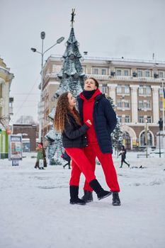 young family guy and girl spend the day in the park on a snowy day. Emotional young couple having fun while walking in the winter city, a lively man hugs his laughing beautiful woman