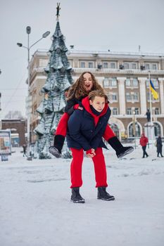 young family guy and girl spend the day in the park on a snowy day. Emotional young couple having fun while walking in the winter city, a lively man hugs his laughing beautiful woman