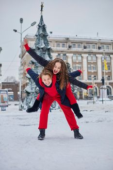 young family guy and girl spend the day in the park on a snowy day. Emotional young couple having fun while walking in the winter city, a lively man hugs his laughing beautiful woman