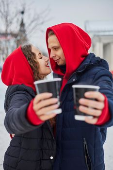 young family guy and girl spend the day in the park on a snowy day. the guy hugs the girl while standing on the street, they drink coffee together