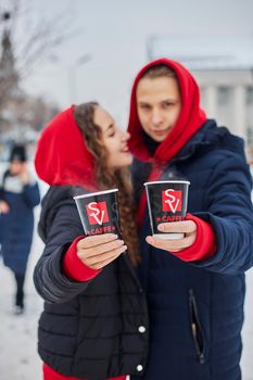 young family guy and girl spend the day in the park on a snowy day. the guy hugs the girl while standing on the street, they drink coffee together