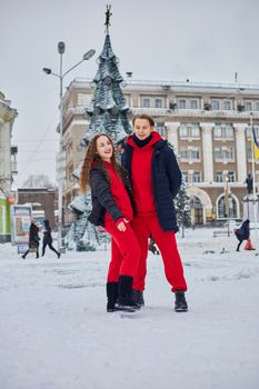 young family guy and girl spend the day in the park on a snowy day. Emotional young couple having fun while walking in the winter city, a lively man hugs his laughing beautiful woman