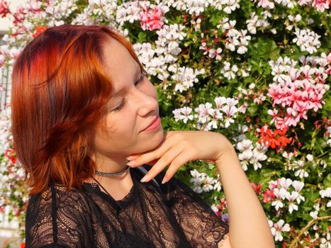 portrait of a smiling red-haired teenage girl with closed eyes on a floral background in the sunlight.