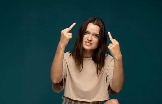 Portrait of brunette student woman showing middle finger doing rebel expression at camera standing in studio with blue background