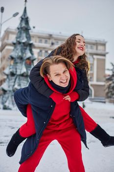 young family guy and girl spend the day in the park on a snowy day. Emotional young couple having fun while walking in the winter city, a lively man hugs his laughing beautiful woman