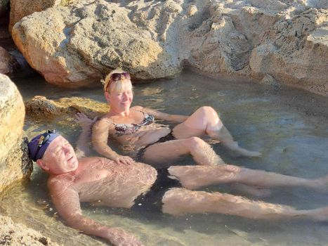 balneotherapy, a man and a woman lie in a natural mineral water between stones in the sunlight.