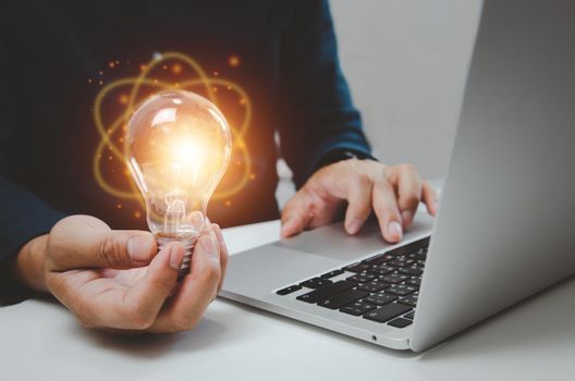 Hand man holding bulb light idea creativity inspiration and using computer laptop on desk.
