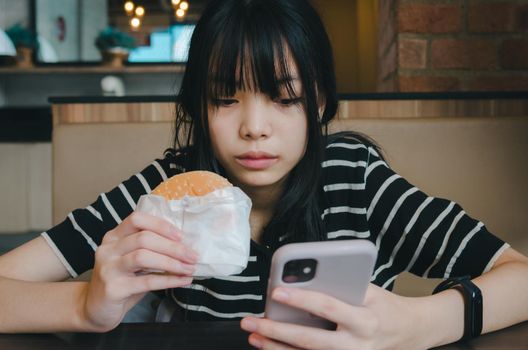 Female person holding mobile smartphone social network internet technology and eat hamburger fast food.
