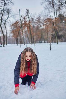 a young happy woman is having fun in a winter park, throwing snow, it is cold in her hands, the emissions are off scale