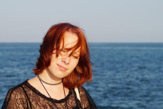 portrait of a smiling red-haired teenage girl against the backdrop of the sea.