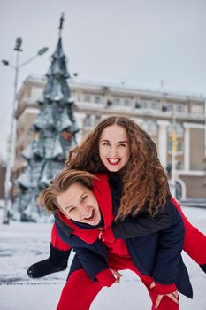 young family guy and girl spend the day in the park on a snowy day. Emotional young couple having fun while walking in the winter city, a lively man hugs his laughing beautiful woman