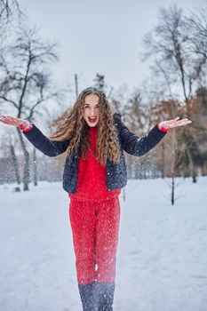 a young happy woman is having fun in a winter park, throwing snow, it is cold in her hands, the emissions are off scale