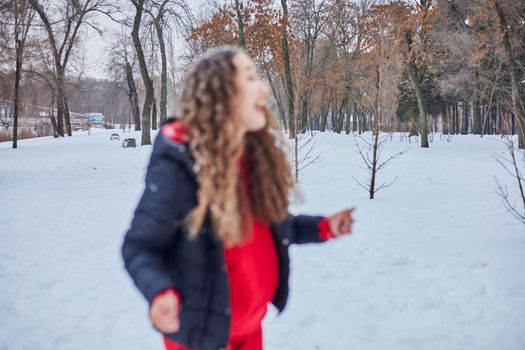 a young happy woman is having fun in a winter park, throwing snow, it is cold in her hands, the emissions are off scale