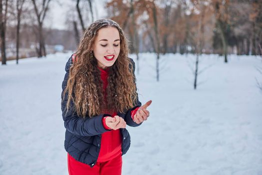 a young happy woman is having fun in a winter park, throwing snow, it is cold in her hands, the emissions are off scale