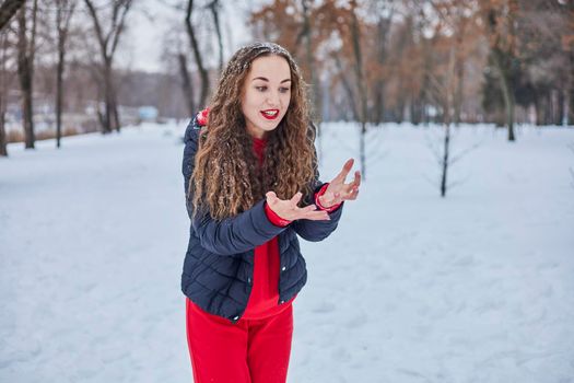 a young happy woman is having fun in a winter park, throwing snow, it is cold in her hands, the emissions are off scale