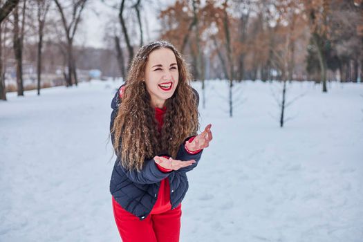 a young happy woman is having fun in a winter park, throwing snow, it is cold in her hands, the emissions are off scale