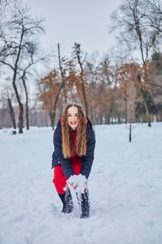 a young happy woman is having fun in a winter park, throwing snow, it is cold in her hands, the emissions are off scale