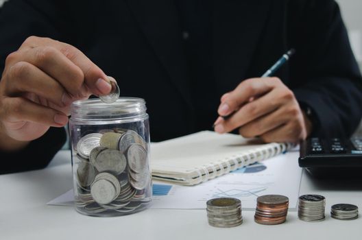 businessman is shown holding a jar with coins for savings and investments. Concept of tax payments and business accounting.