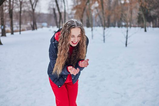 a young happy woman is having fun in a winter park, throwing snow, it is cold in her hands, the emissions are off scale