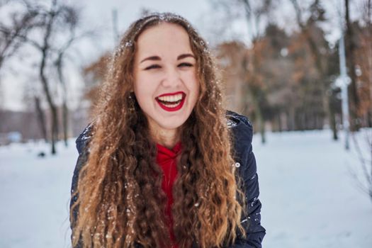 a young happy woman is having fun in a winter park, throwing snow, it is cold in her hands, the emissions are off scale