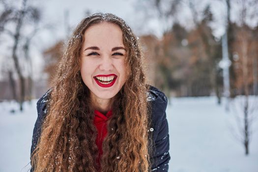 a young happy woman is having fun in a winter park, throwing snow, it is cold in her hands, the emissions are off scale