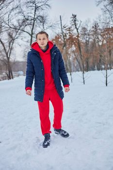 a young happy man is having fun in a winter park, throwing snow, it is cold in his hands, the emissions are off scale