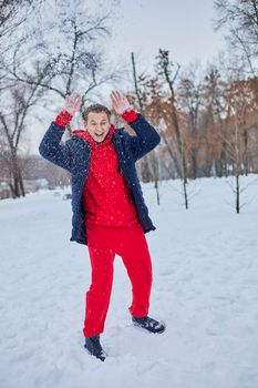 a young happy man is having fun in a winter park, throwing snow, it is cold in his hands, the emissions are off scale