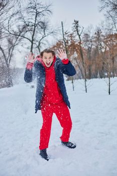 a young happy man is having fun in a winter park, throwing snow, it is cold in his hands, the emissions are off scale