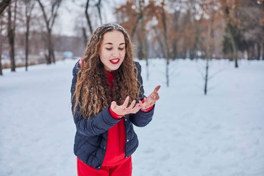 a young happy woman is having fun in a winter park, throwing snow, it is cold in her hands, the emissions are off scale