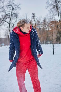 a young happy man is having fun in a winter park, throwing snow, it is cold in his hands, the emissions are off scale