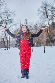 a young happy woman is having fun in a winter park, throwing snow, it is cold in her hands, the emissions are off scale