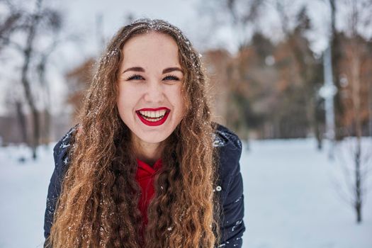 a young happy woman is having fun in a winter park, throwing snow, it is cold in her hands, the emissions are off scale