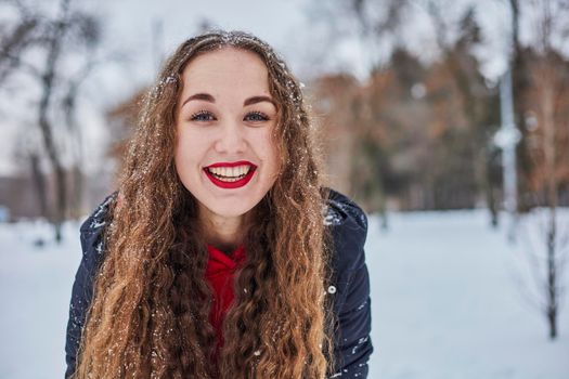 a young happy woman is having fun in a winter park, throwing snow, it is cold in her hands, the emissions are off scale